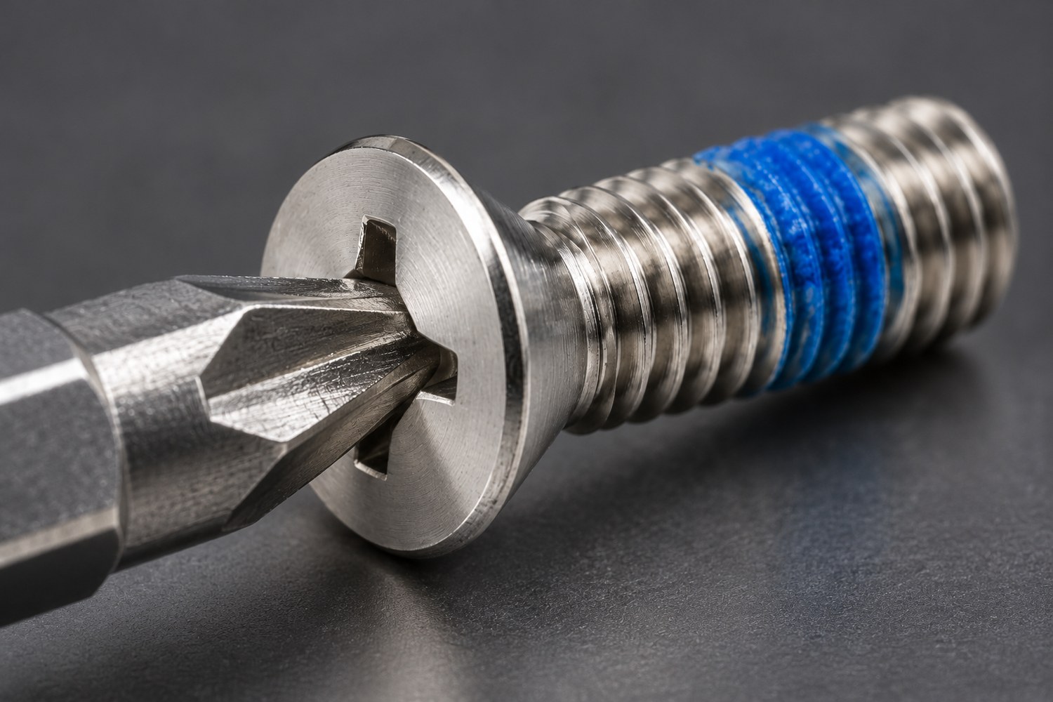 Phillips driver bit engaged in the cross recess of a small stainless countersunk screw, showing wall contact